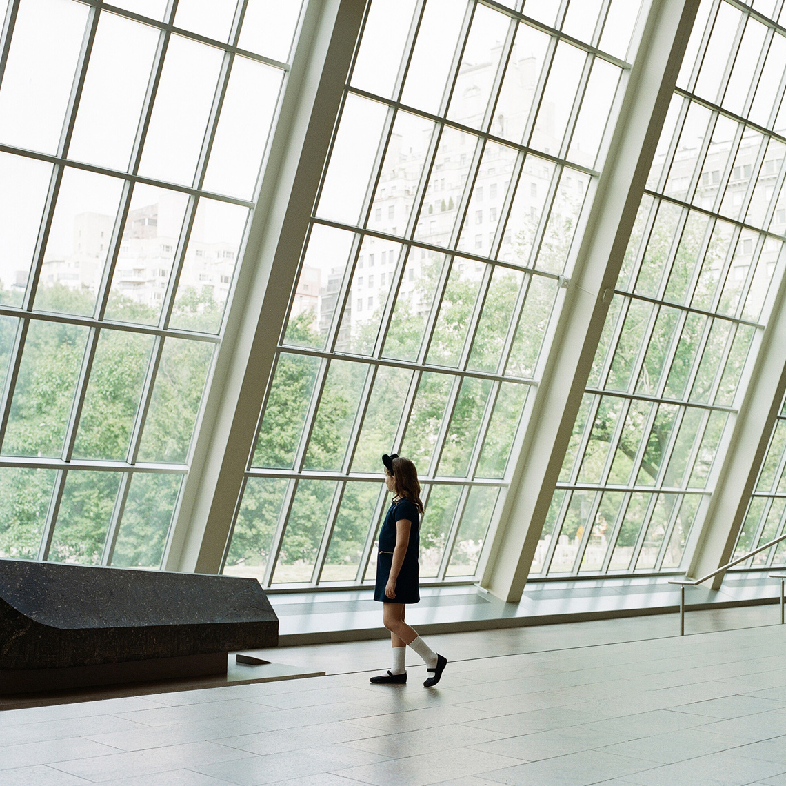 young girl navy dress walking Met Museum New York floor to ceiling windows editorial photography