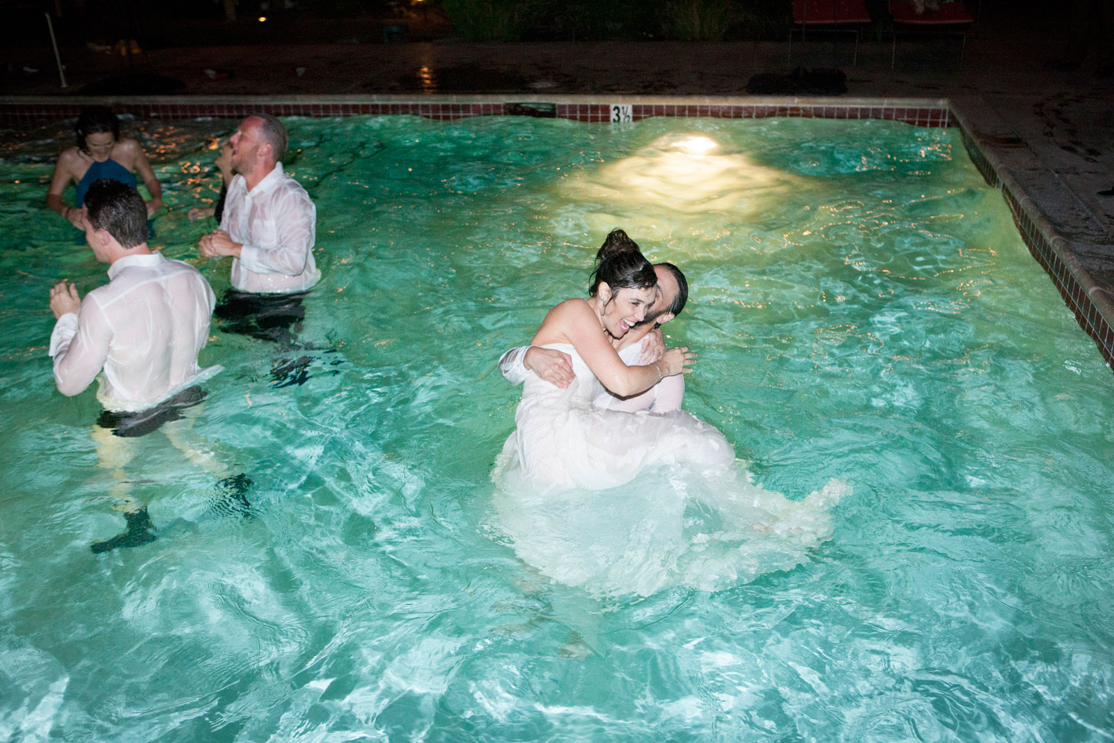 Bride in wedding dress wading in pool with attendants, editorial luxury wedding photography