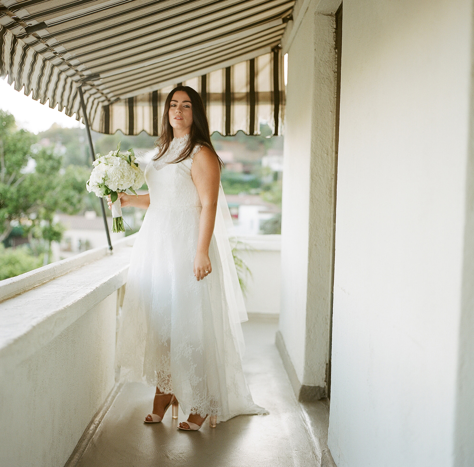 Bride in white dress on Chateau Marmont terrace with striped awning, luxury wedding photography