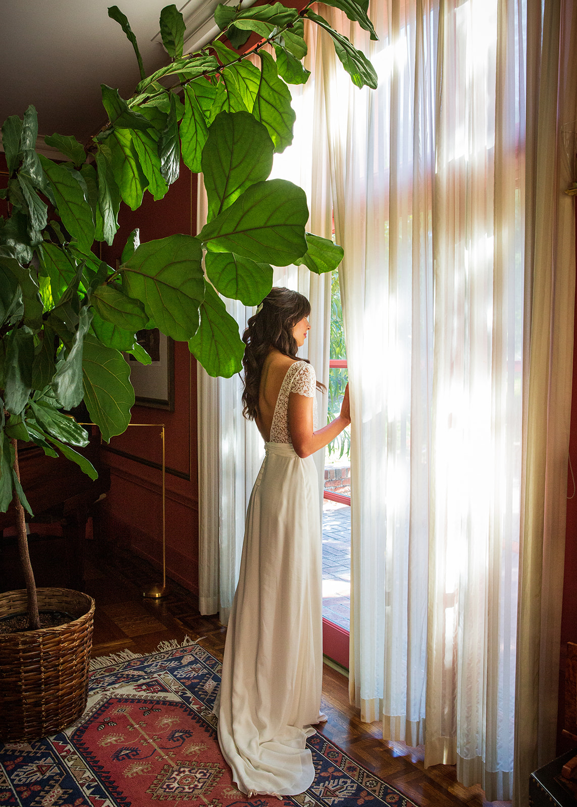 Bride in white gown beside fiddle leaf fig tree in warm window light, luxury interior lifestyle photography
