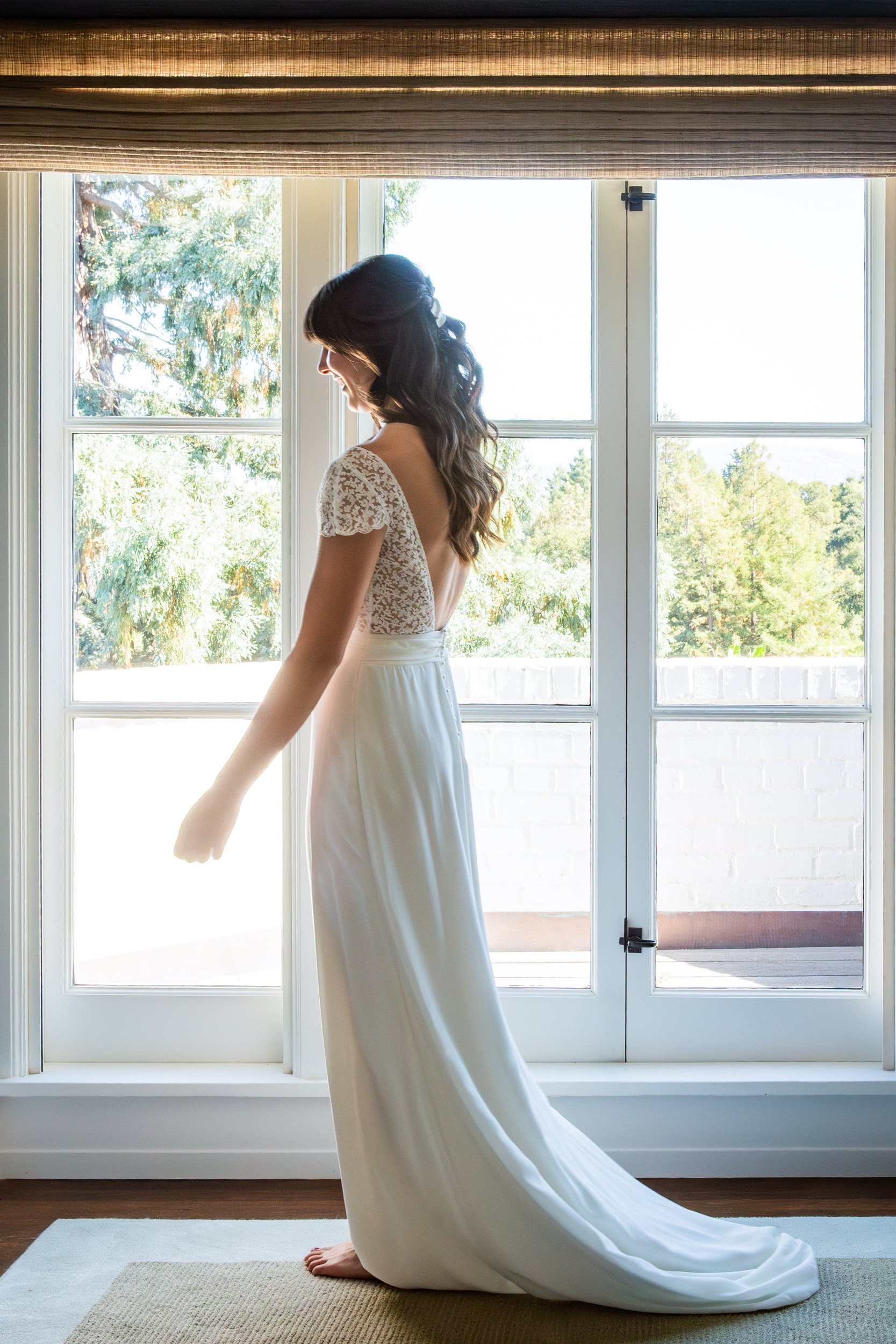 Bride in white gown standing at tall French windows with golden afternoon light, luxury estate photography
