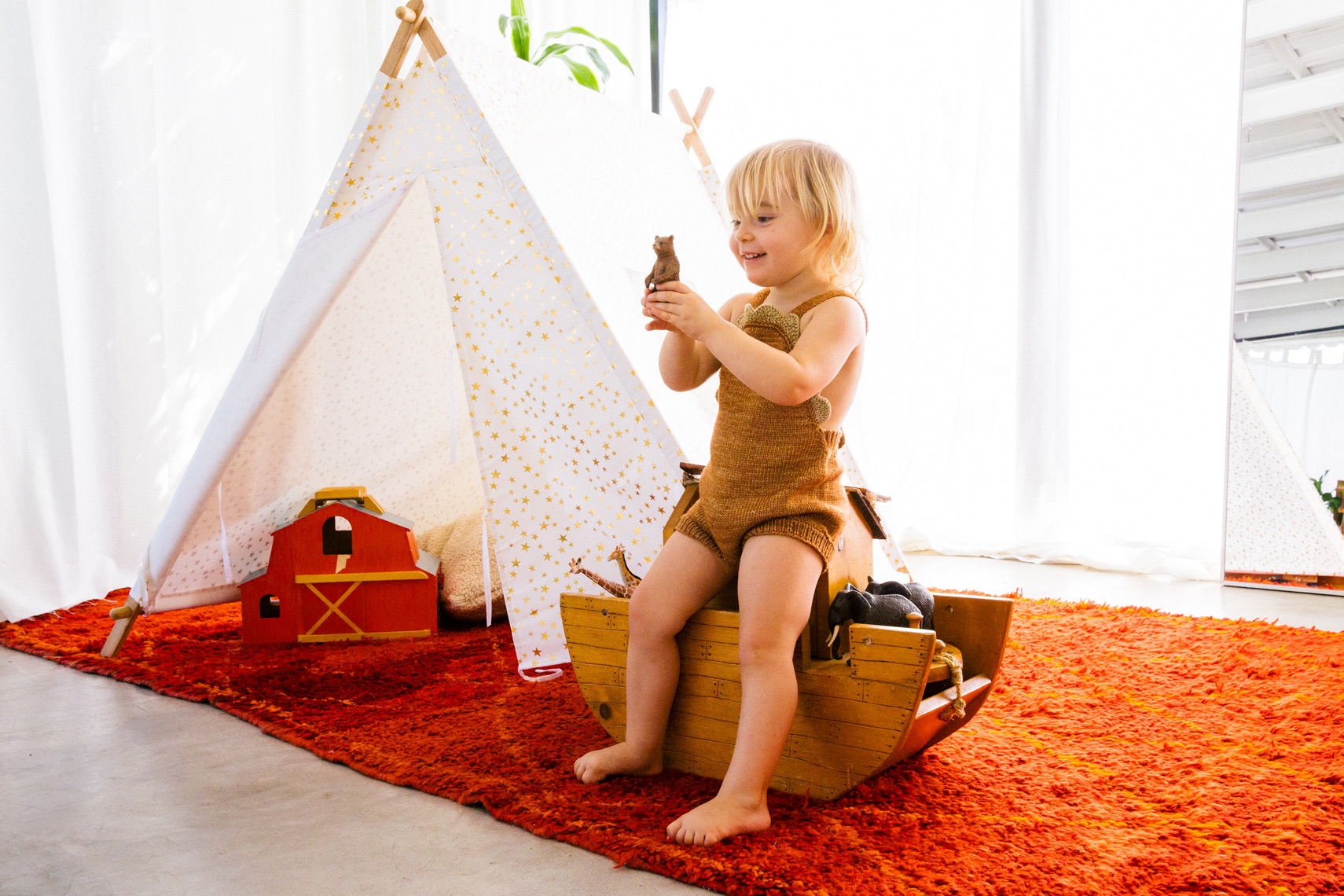 Child on bed beside teepee in styled children