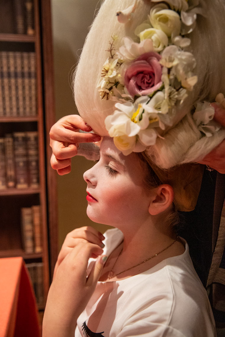 Child wearing elaborate floral headpiece beside books, editorial portrait photography