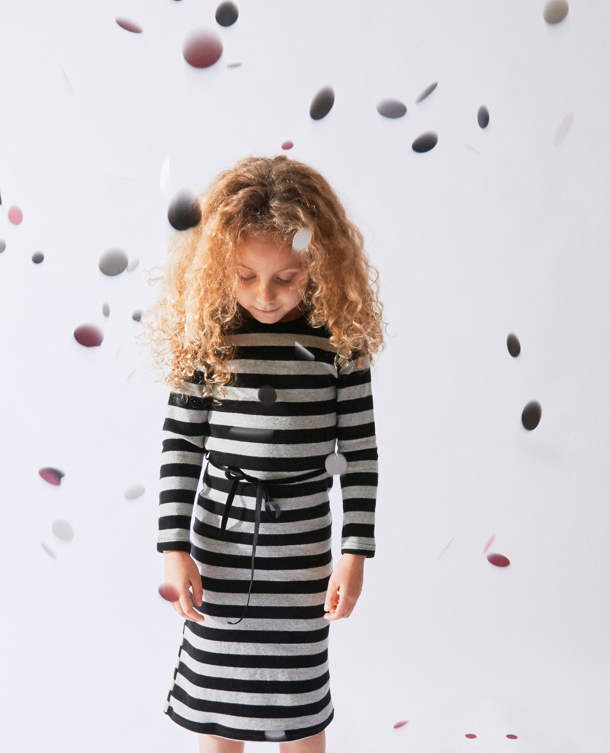 Child in striped dress with falling confetti on white background, children