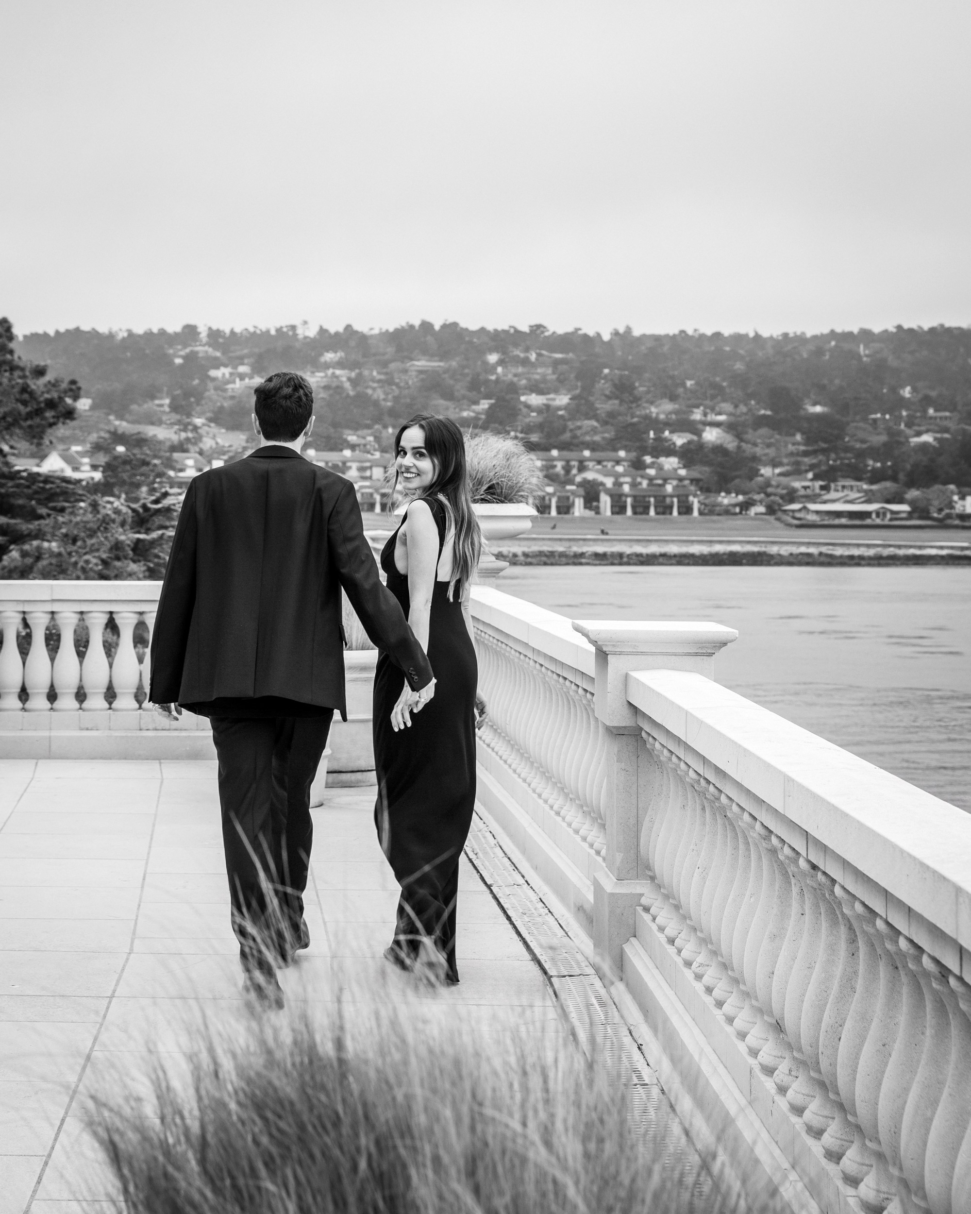 Couple walking away on stone balustrade terrace overlooking Pebble Beach bay, luxury editorial photography