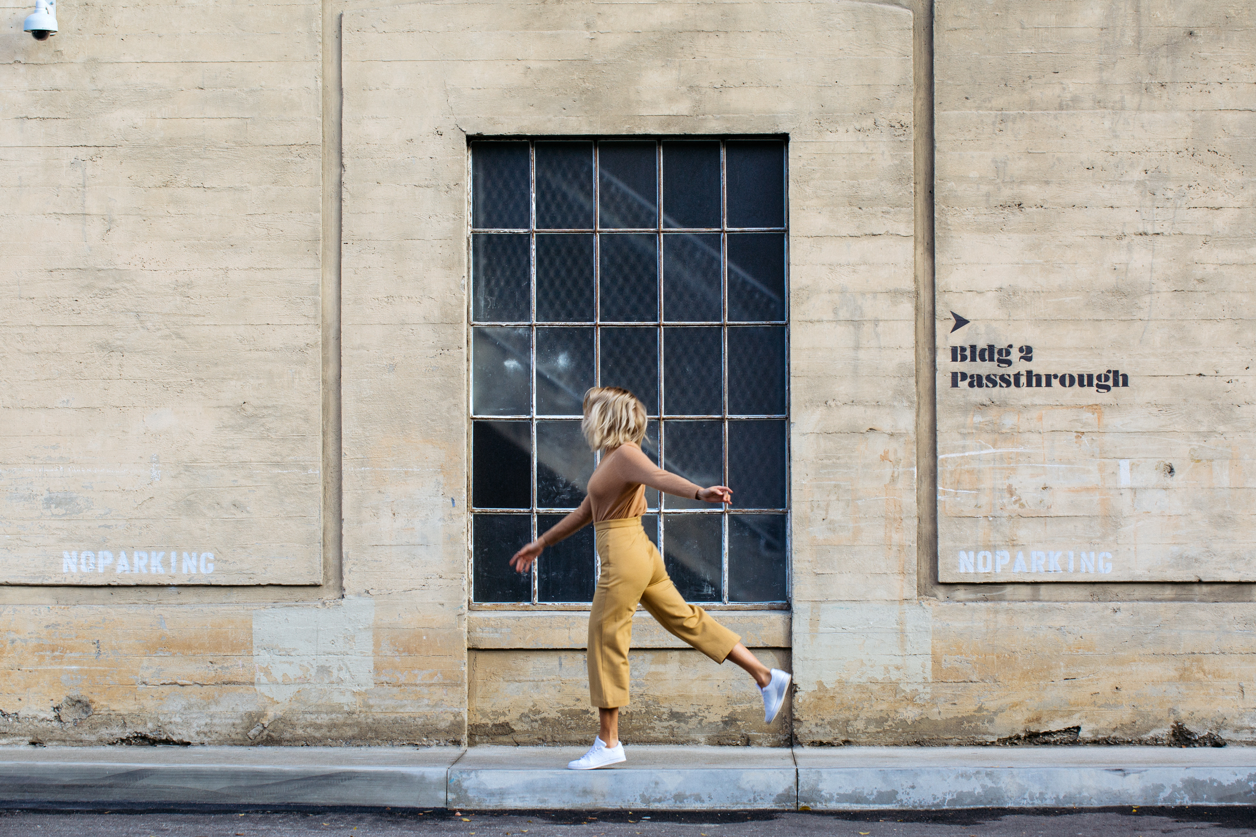 Woman in yellow jumpsuit walking past industrial concrete wall, Los Angeles editorial lifestyle photography