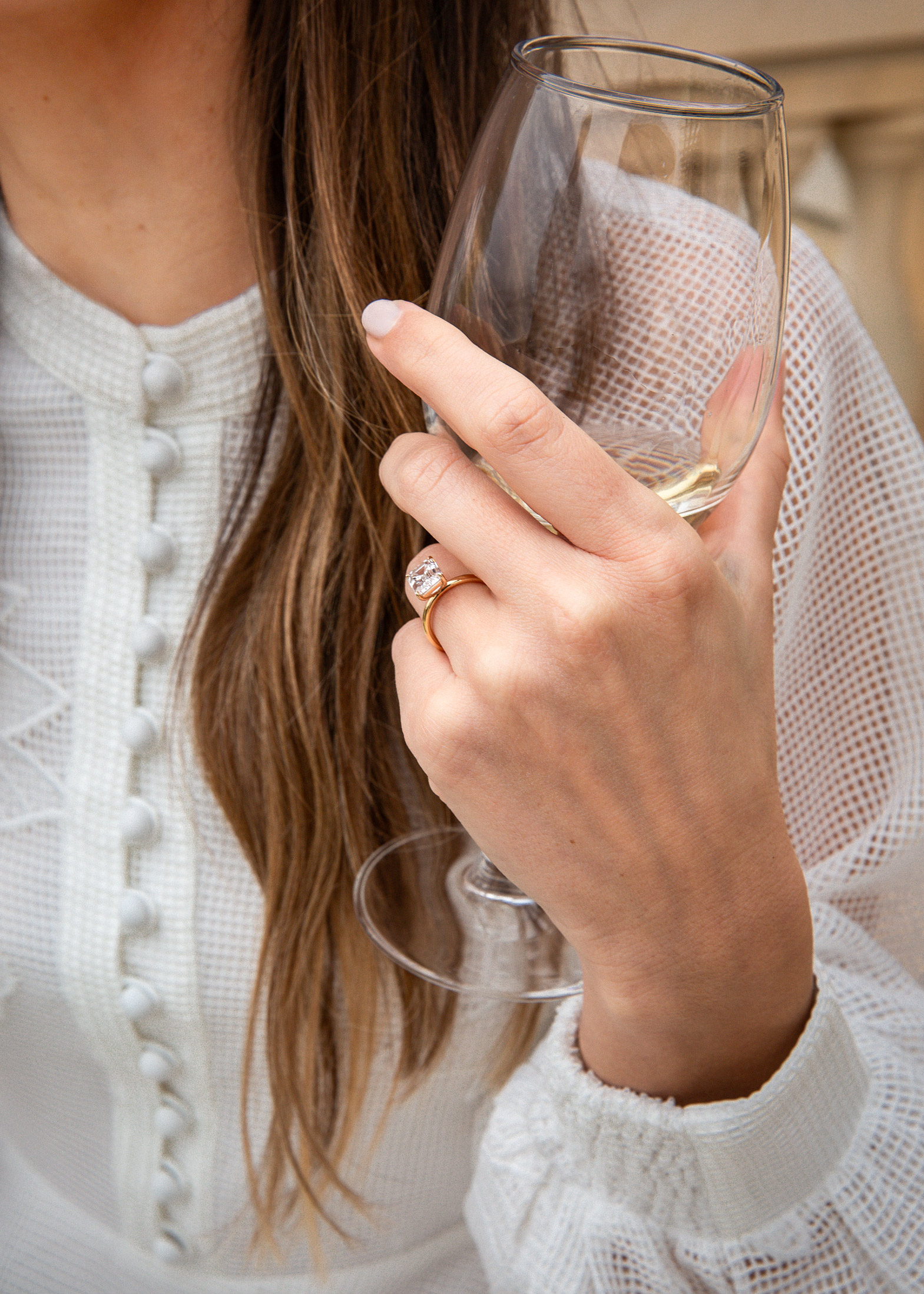 Hand with engagement ring holding champagne glass in white lace sleeve, luxury lifestyle detail photography