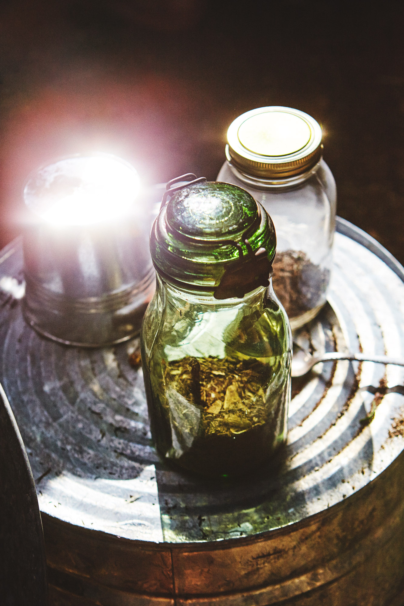 Glass mason jars with glowing light on metal tray against dark background, editorial still life photography