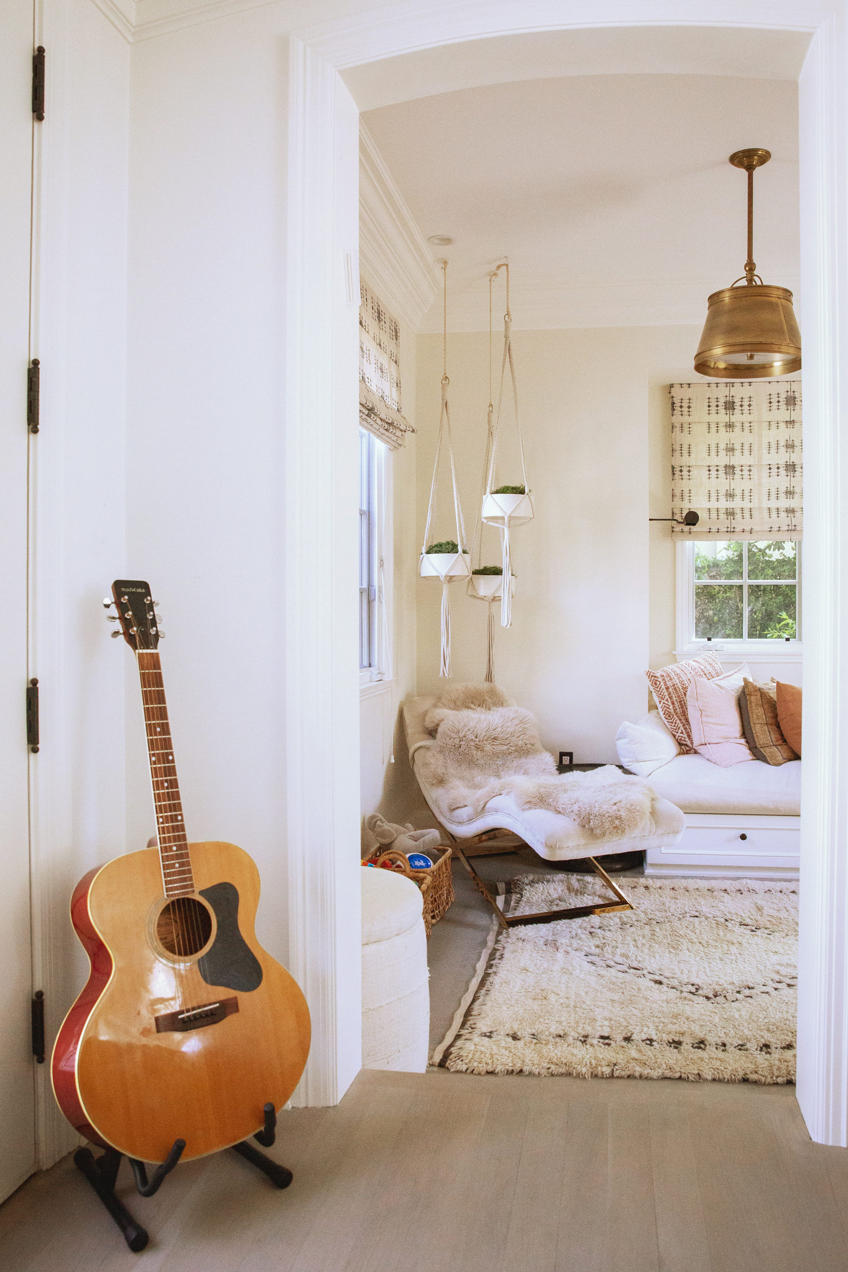 Acoustic guitar leaning against white wall in bright airy living room, lifestyle interior photography