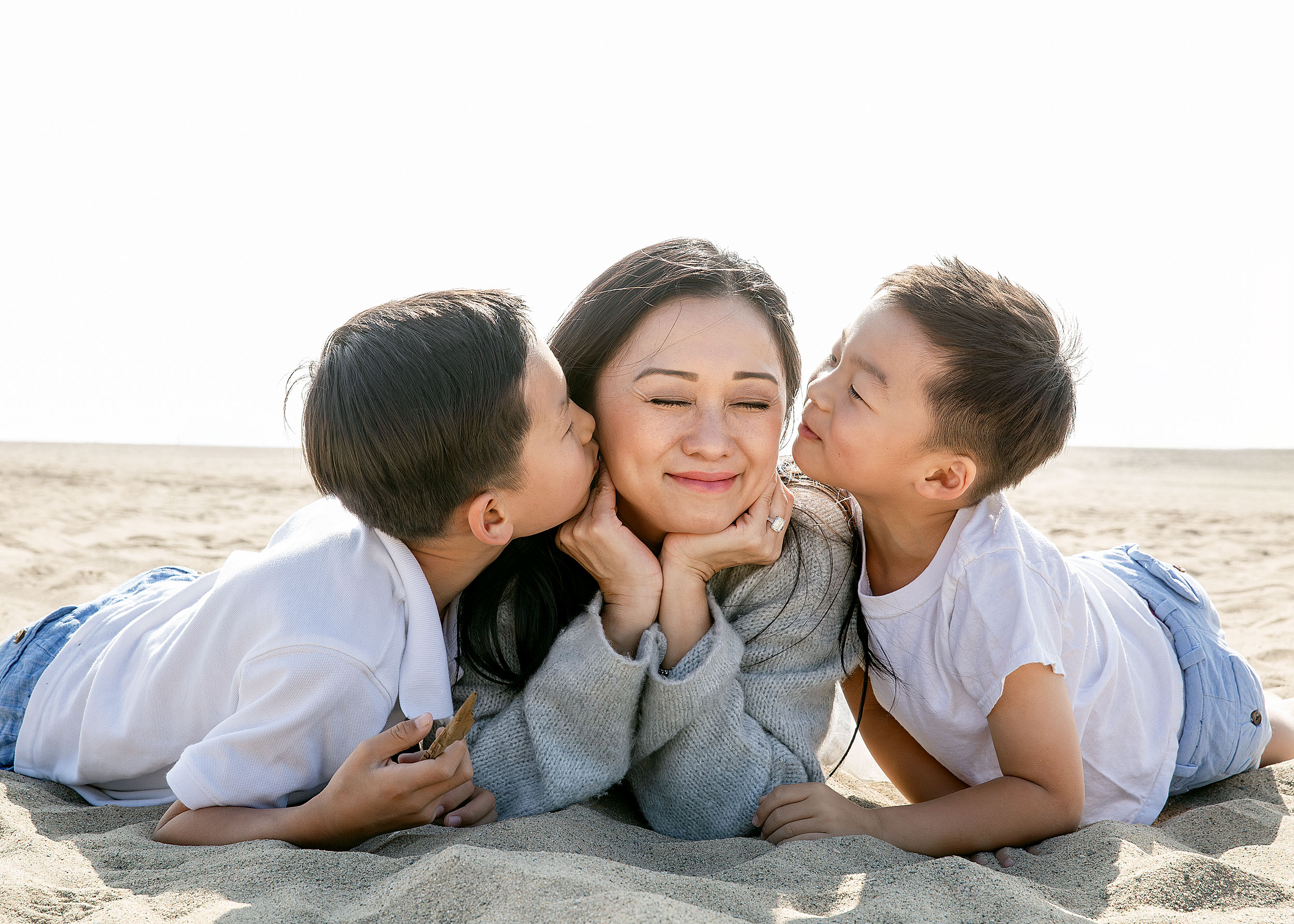 mother laughing as two sons kiss her cheeks simultaneously beach candid lifestyle editorial photography
