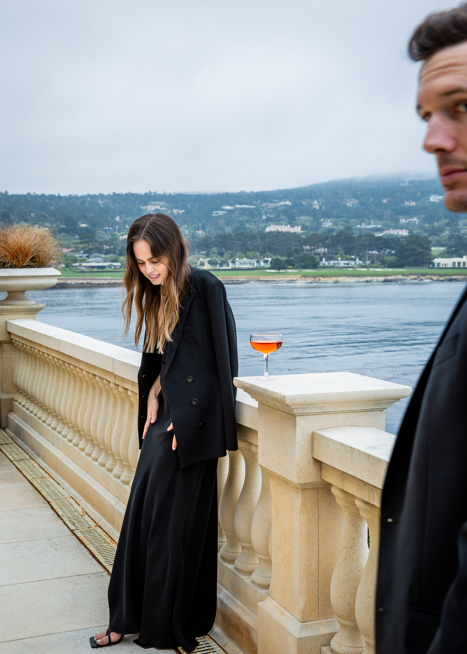 Woman in black oversized blazer on stone terrace with aperol coupe, coastal fog and bay views, Pebble Beach luxury lifestyle photography