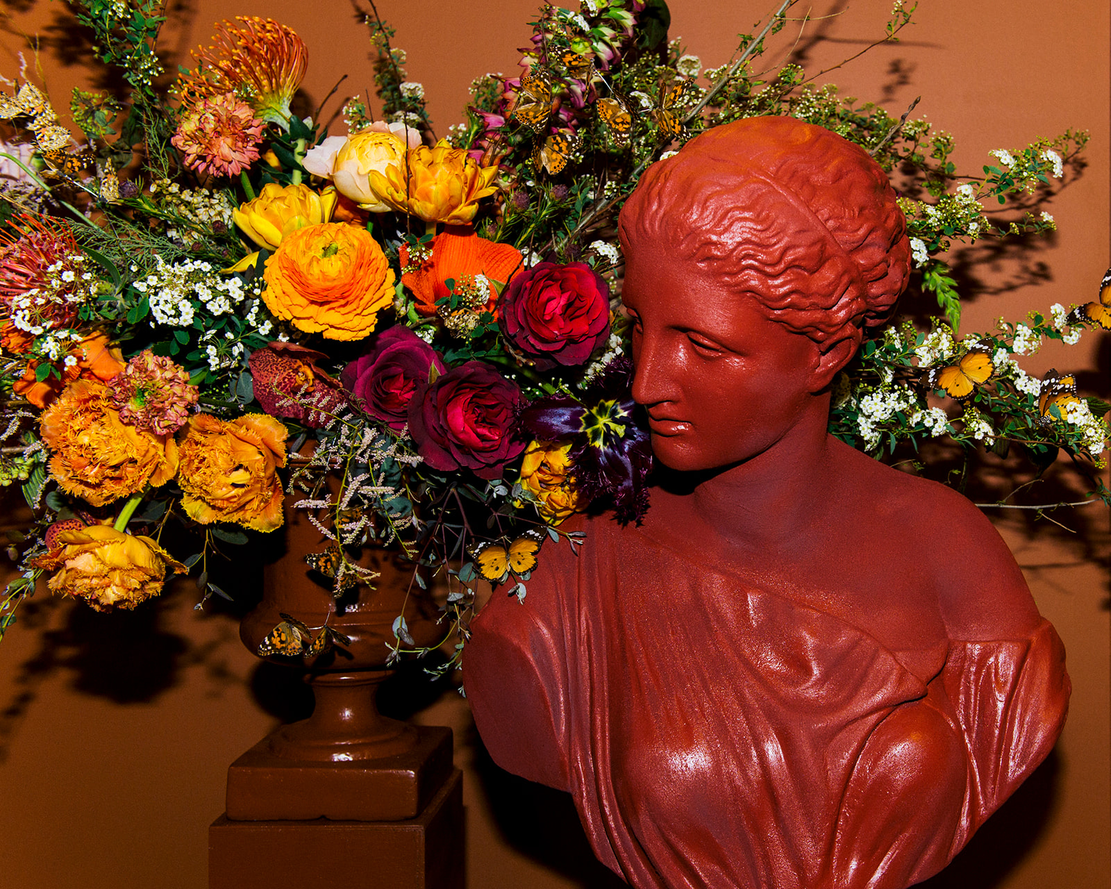 Red classical bust sculpture with colorful floral arrangement, luxury editorial photography