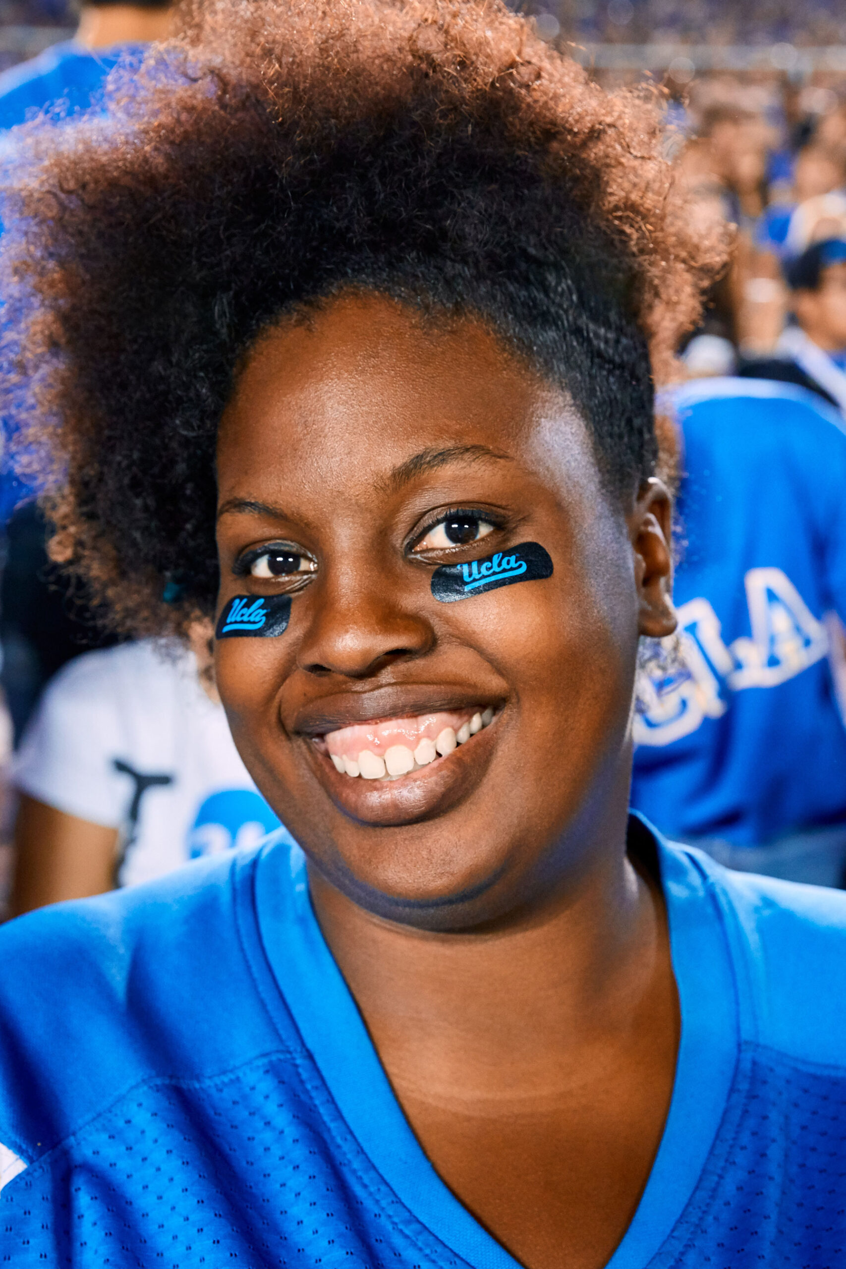 UCLA student with blue face paint smiling at gameday, brand event portrait photography