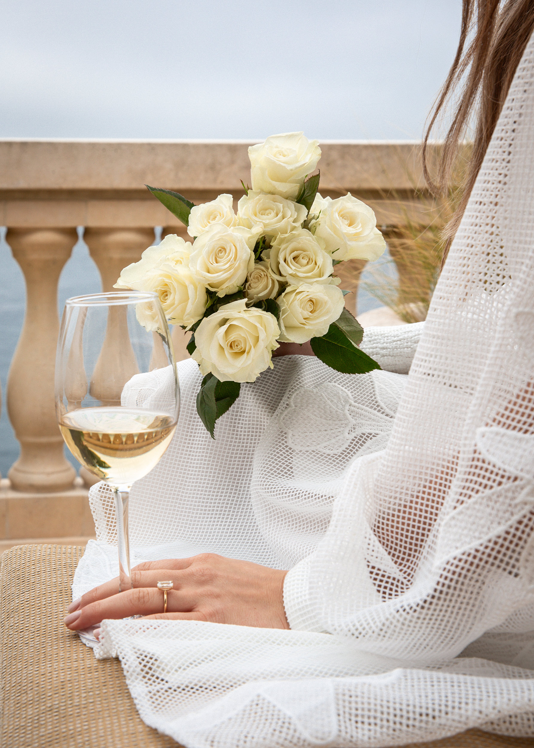 White roses bouquet with wine glass on stone terrace overlooking Pebble Beach bay, luxury lifestyle detail photography
