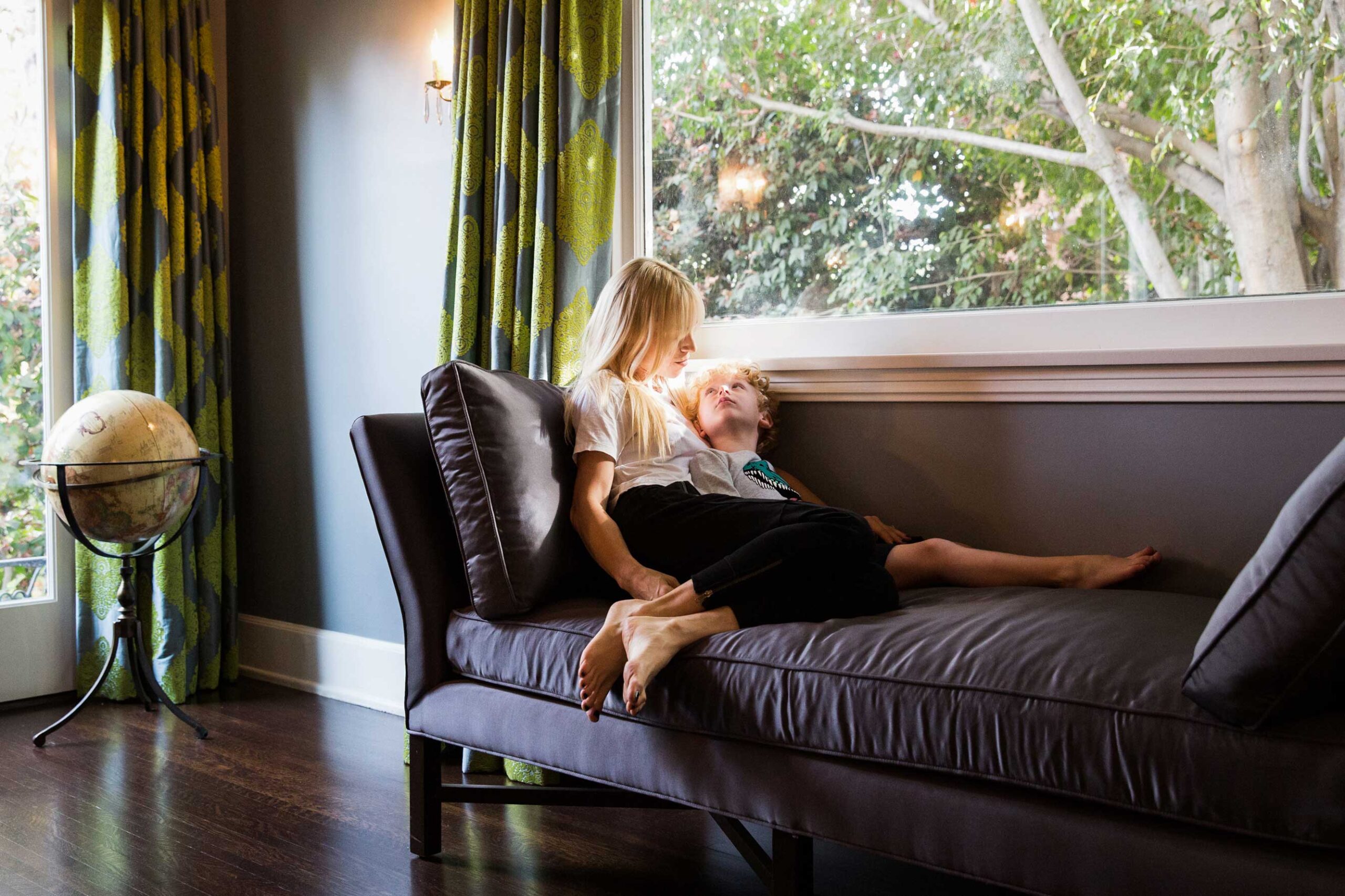 Woman reading on sofa by large window with natural light and globe, interior lifestyle photography