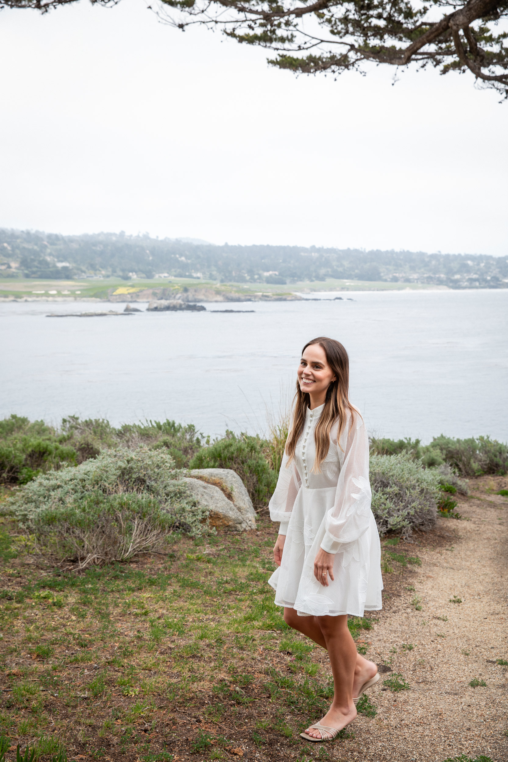 Woman in white dress on coastal path surrounded by coastal sage, Pebble Beach luxury lifestyle photography