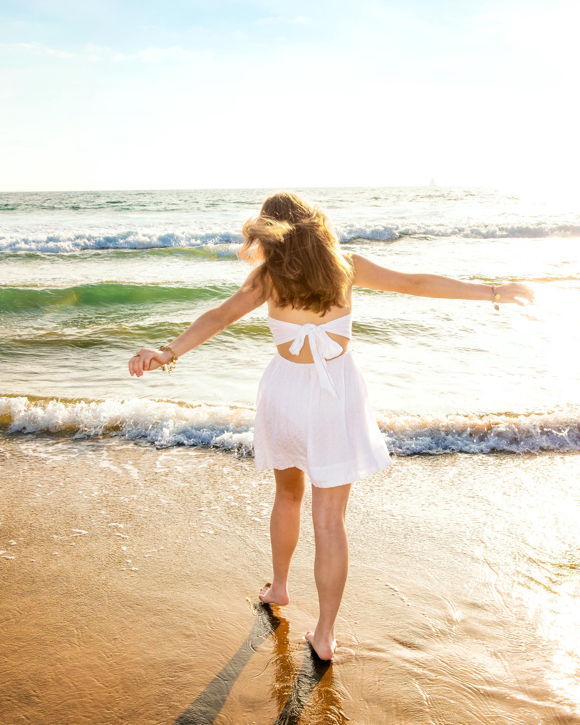woman in white dress arms outstretched ocean waves coastal lifestyle editorial photography